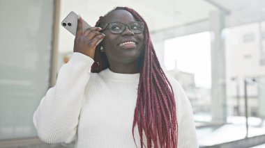 Neşe saçı örgülü Afro-Amerikan bir kadın şehrin caddesinde dikilirken telefonla konuşuyor..