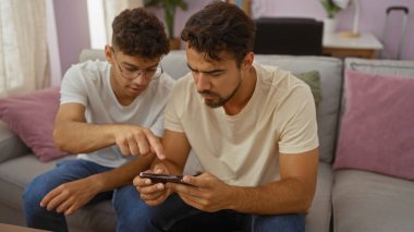Baba ve oğul oturma odasında bir kanepede oturuyor, birlikte telefona bakıyorlar, sevgiyle ve odaklanarak, İspanyol erkekler arasındaki bağı gösteriyorlar..