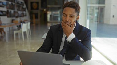 Ofis ortamında yakışıklı bir genç, düşünceli bir şekilde dizüstü bilgisayara bakıyor, işe yoğunlaşmayı öneriyor..