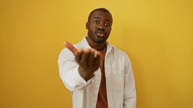 Sarı arka planı olan genç adam çekici bir ifade sergiliyor. Ayırt edici hareketler yapıyor..