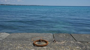 Salento, Puglia, İtalya 'da güneşli bir gökyüzünün altında porto sezaryenin berrak mavi sularına bakan bir iskeledeki paslı halka..