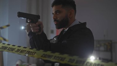 Odaklanmış bir adam, loş bir odada suç mahalli bandının ötesine silah doğrultuyor..