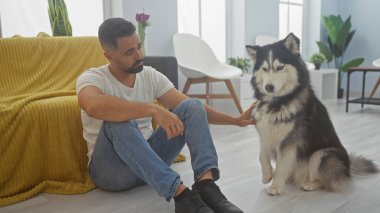 Yakışıklı, genç, İspanyol bir adam, modern bir evin parlak oturma odasında bir Husky ile iletişim kuruyor..