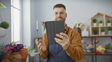 Çiçekçide sakallı genç bir adam elinde bir tablet tutuyor. Etrafı bitki ve çömleklerle çevrili. Girişimciliği temsil ediyor..
