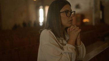 A young hispanic woman prays in a beautiful, historic church in italy, with a serene and reflective atmosphere illuminated by gentle candlelight. clipart