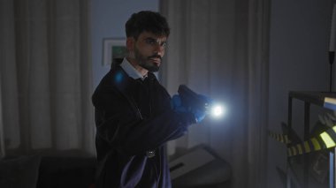 Sakallı genç bir İspanyol, el feneriyle kapalı bir suç mahallini arıyor.