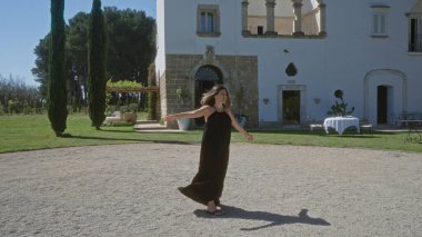 Siyah elbiseli genç bir İspanyol kadın Puglia 'da güzel bir İtalyan villasının önünde neşeli bir şekilde dönüyor. Etrafı yemyeşil bahçeler ve güneşli bir günde yükselen selvi ağaçları ile çevrili..