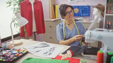 Neşeli bir İspanyol kadın renkli kumaşlar ve dikiş makinesiyle aydınlık bir atölyede terzilik yapmaktan zevk alıyor..