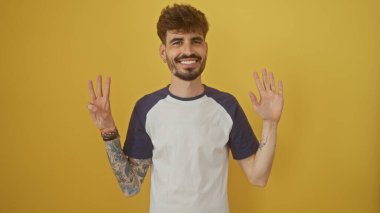 Yakışıklı sakallı adam sarı arka planda izole edilmiş sekiz numaralı hareketi yapıyor.