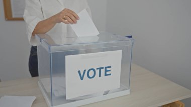 Adult woman casting ballot in a polling station indoors during elections clipart