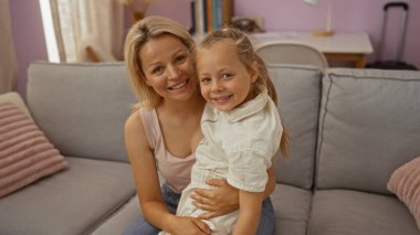 Anne ve kız, sarı saçlı, rahat bir oturma odasında birlikte gülümseyen, kitaplarla ve yastıklarla çevrili, sıcak bir aile bağı sergiliyor..