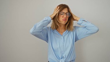 Kadın, elleri başının üstünde, gözlüklü ve mavi gömlekli, beyaz arka planda izole bir şekilde stresli hissediyor.