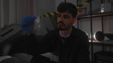 Genç bir İspanyol, arka planda uyarı bandıyla loş ışıkta aydınlatılmış bir suç mahallindeki kanıtları inceliyor..