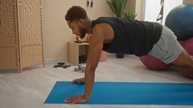 Spor salonundaki paspasın üzerinde egzersiz yapan genç adam, arka planda spor ekipmanları olan kapalı bir spor merkezine odaklanıyor ve kararlılığını gösteriyor.