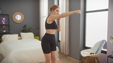 Aktif giyimli genç bir kadın modern yatak odasında boks antrenmanı yapıyor..