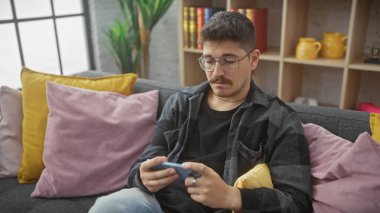 Konsantre olmuş genç bir İspanyol, rahat bir oturma odasındaki kanepede oyun oynuyor.