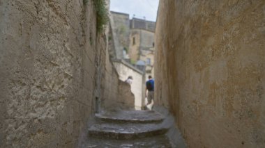 Turistler materyada, bazilikada, İtalya 'da, yaşlanmış taş duvarlarla dolu dar ve tarihi bir ara sokağı keşfederek samimi, otantik bir Avrupa kültürel deneyimi yaratıyorlar..