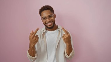 Gözlüklü genç adam, izole edilmiş pembe arka planda gülümseyen orta parmaklarıyla müstehcen bir hareket yapıyor.