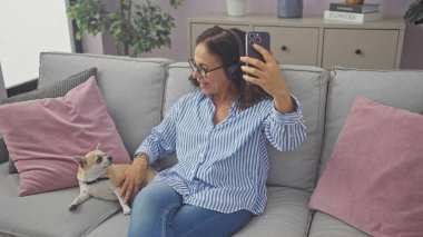 Orta yaşlı bir kadın evcil chihuahua 'sıyla kapalı bir kanepede selfie çekiyor..