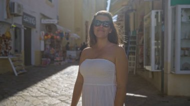 Beyaz elbiseli güzel bir İspanyol kadın Avrupa 'da yaz aylarında parlak güneş ışığıyla aydınlanan Puglia, İtalya' da Gelibolu 'nun büyüleyici sokaklarında yürüyor..
