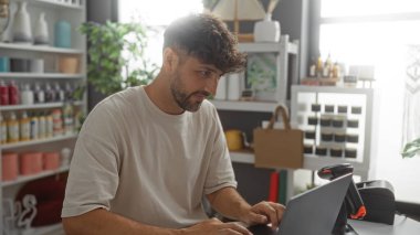 Etrafı çeşitli dekorasyon ve bitkilerle çevrili bir ev dekorasyonu mağazasında çalışan genç adam dizüstü bilgisayardaki görevine odaklandı.