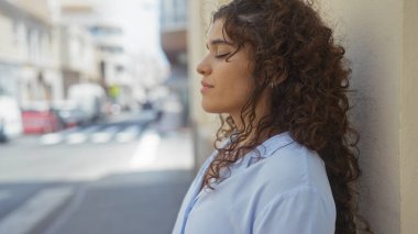 Genç, esmer, güneşli bir şehir sokağında gözleri kapalı duran, hareketli şehir ortamında sakin bir anın tadını çıkaran bir kadın..