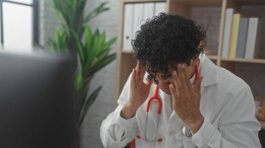 Stresli, labaratuvar önlüklü, kapalı klinikte steteskobu olan genç bir adam.