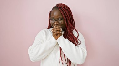 Gülümseyen Afro-Amerikan kadın örgülü gözlüklü ve pembe arka planda beyaz kazak giyiyor..