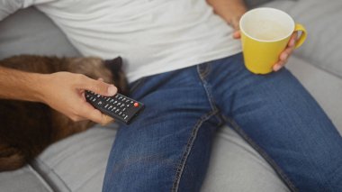 Uzaktan kumandalı ve kupalı bir adam, yanında uyuyan bir kedi..