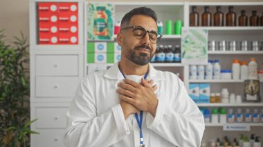 A handsome hispanic man pharmacist stands gratefully in an indoor pharmacy with shelves of medicine. clipart