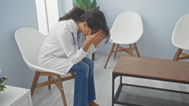 Stresli kadın doktor bir klinikte oturuyor, sağlık çalışanlarının bitkinliğini ve duygusal sıkıntılarını gösteriyor..