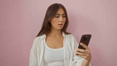 Tecrit edilmiş pembe arka planda genç, çekici esmer kadın endişeli bir ifadeyle akıllı telefona bakıyor.