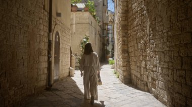 Genç bir İspanyol kadın, Bari 'nin Puglia, İtalya' daki eski kasabasının dar, taşlarla döşenmiş sokaklarında yürüyor. Güneşin tadını çıkarıyor..