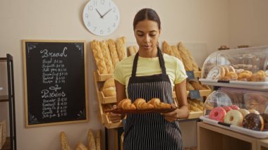 Woman holding croissants in a bakery setting with bread and pastries displayed in the background while she stands in front of a chalkboard menu and clock clipart