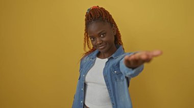Sarı arka planda elini uzatan kendinden emin Afrikalı genç bir kadın.