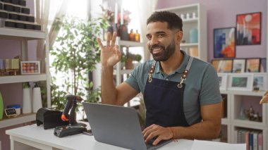 Delikanlı ev dekorasyonu mağazasında dizüstü bilgisayarla çalışırken el hareketi yapıyor.