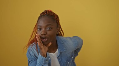 Kotlu genç Afrikalı Amerikalı kadın izole edilmiş sarı bir arka plana karşı fısıldıyor. Gizlilik ve günlük yaşam tarzını somutlaştırıyor..