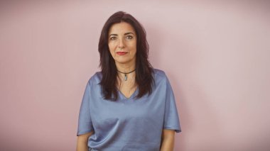 Olgun İspanyol bir kadın pembe bir arka plana karşı özgüvenle duruyor, zarafet ve özgüven saçıyor..