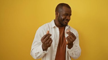 Genç adam, elleri ile izole edilmiş sarı bir arkaplan üzerinde para hareketi yapıyor, zenginlik ve güveni gösteren bir ifade..