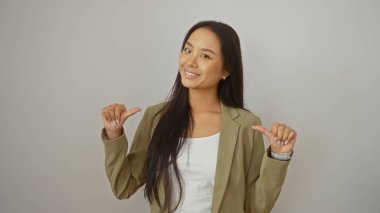 Genç Çinli bir kadın beyaz bir arkaplan önünde kendine güvenle gülümseyen bir ceket giyerken kendini işaret ediyor.