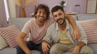 Sıcak bir oturma odasında birbirini kucaklayan iki gülümseyen adam, yakın dostluğu ya da aile bağını simgeliyor..