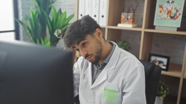 Hastanedeki sakallı genç Arap adam laboratuvar önlüğü giyiyor ve bilgisayarının başında çalışıyor..