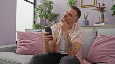 Modern bir oturma odasında akıllı telefonu elinde tutan yakışıklı bir adam.