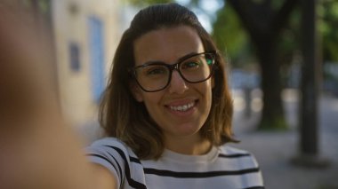 Genç İspanyol bir kadın ders sırasında selfie çekiyor. Puglia, İtalya 'da bir kasaba. Gözlük takıyor ve çizgili bir gömlek giyiyor..