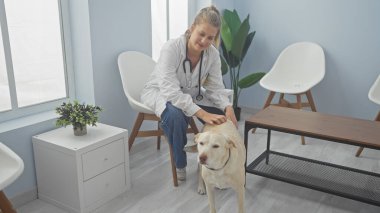 Klinikteki genç bayan veteriner, parlak bir veteriner bekleme odasında dost canlısı bir köpeği okşuyor.