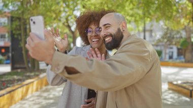 Şehir parkında akıllı bir telefonla selfie çeken mutlu ırklar arası bir çift şehir hayatını ve modern ilişkileri gözler önüne seriyor..