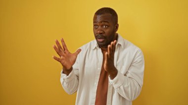 İzole edilmiş sarı arka planda duygularını ifade eden genç bir adam. Elleri havada, gündelik bir tişört giyiyordu.