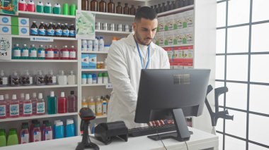 Yakışıklı genç adam, iyi stoklanmış bir eczanede çeşitli ilaç ve sağlık ürünleri bulunan bir bilgisayarda özenle çalışıyor..