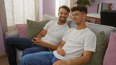 Baba ve oğul rahat bir oturma odasında rahat bir kanepede birlikte gülümsüyor, güçlü bir aile bağı ve sevgi sergiliyorlar.