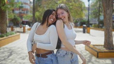 Güneşli bir şehir parkında kucaklaşan iki gülen kadın